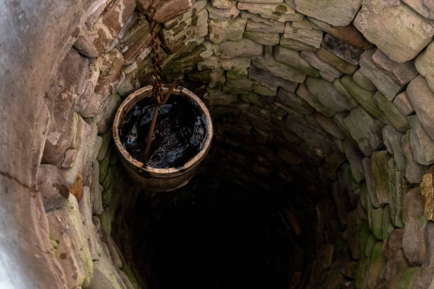 Interior de pozo antiguo de piedra con cubo de madera y agua oscura que necesita desinfección